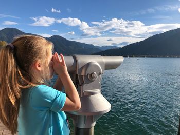 Close-up of girl looking through coin-operated binoculars mountains and sky