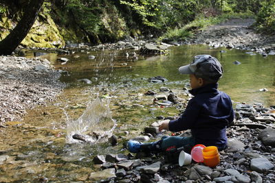 Boy splashing water with rock at forest