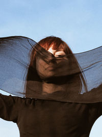 Low angle portrait of young woman holding scarf standing against clear sky