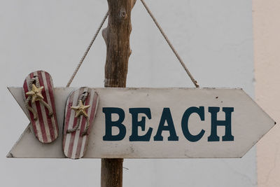 Close-up of sign board hanging on wooden post at beach