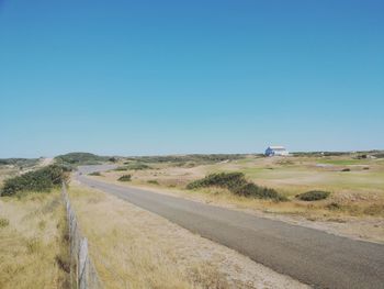 Road amidst field against clear blue sky