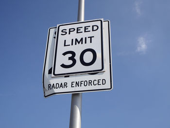 Low angle view of road sign over pole against blue sky