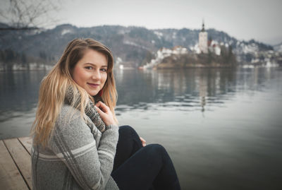 Portrait of woman smiling while sitting on pier over lake during winter