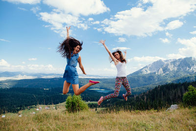 Full length of happy friends jumping over landscape against sky