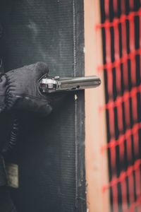 Cropped hand of burglar holding hand gun by door