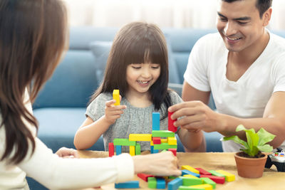 Smiling girl and parents playing with toy blocks in living room at home