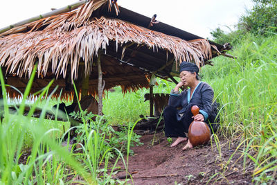 Full length of female farmer sitting by hut on field