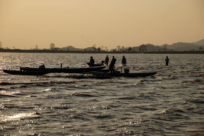 Silhouette people in sea against sky during sunset