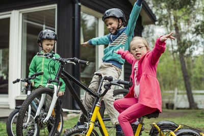 Portrait of girl with arms outstretched riding bicycle with brothers in lawn