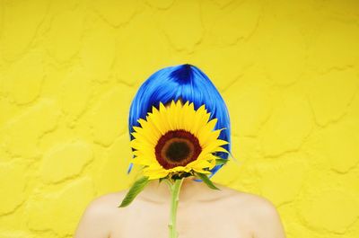 Woman covered with sunflower against yellow background