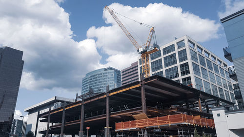 Low angle view of crane by building against sky