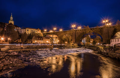 Illuminated city by river against sky at night