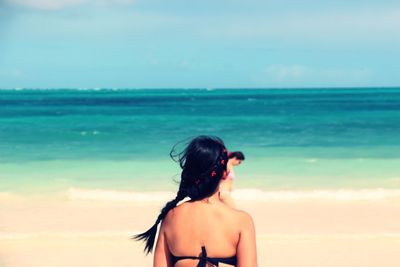 Rear view of woman standing at beach against sky