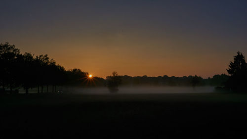 Silhouette trees on field against sky during sunset