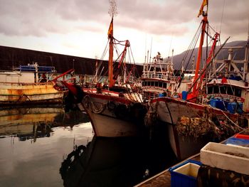 Boats in harbor against cloudy sky