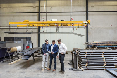 Three men standing on factory shop floor looking at tablet