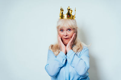 Portrait of senior woman wearing crown against white background