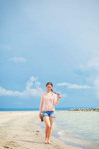 Young brunette woman in a hat, short denim shorts and a pink sweater is walking 