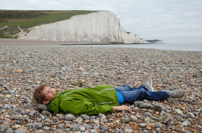 Full length of young man lying on pebbles at beach