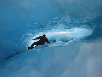 Rear view of man climbing on ice cave