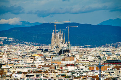 High angle view of townscape and silhouette of sagrada familia against sky, barcelona 