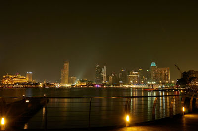 Illuminated buildings by river against sky at night