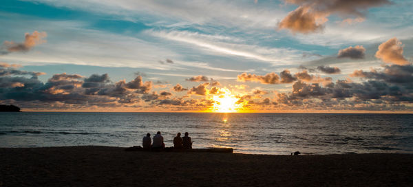 Silhouette people on beach against sky during sunset