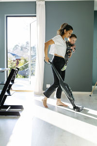 Mother vacuum cleaning while carrying toddler son