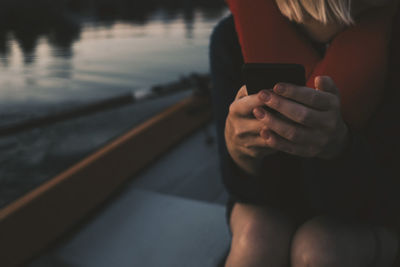 Midsection of woman using mobile phone while sitting in boat on lake