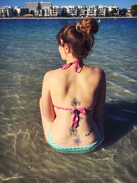 Rear view of young woman in bikini sitting at beach