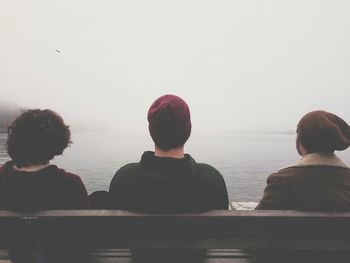 Brothers sitting on wooden bench by lake during foggy weather