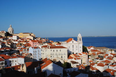 Cityscape by sea against clear blue sky