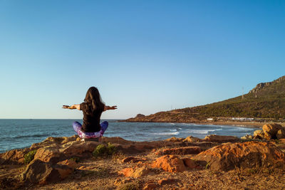 Woman on rock at beach against clear sky