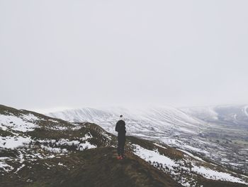 Rear view of man standing on snowcapped mountain against sky