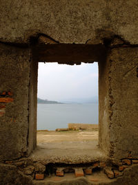 Old ruin building against sky seen through window