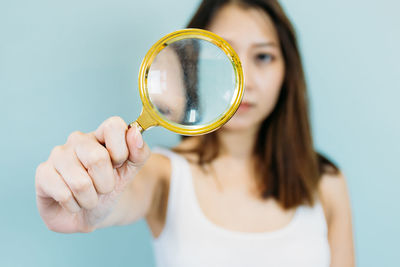 Close-up of young woman holding magnifying glass against blue background