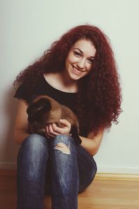 Portrait of happy beautiful woman with cat sitting on hardwood floor against wall