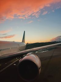 Airplane flying over airport against sky during sunset