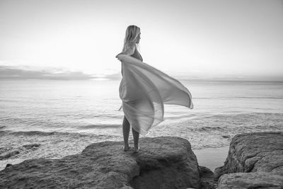 Rear view of woman standing at beach against clear sky