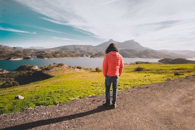 Rear view of woman standing on land by lake against mountains and sky