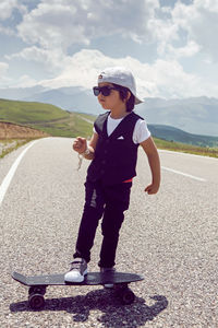 Fashionable child boy in white cap sneakers and vest stands with a skate, road mountains  everest 