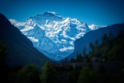 Low angle view of snowcapped mountains against clear blue sky