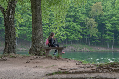 Girl sitting on bench  by lake in forest