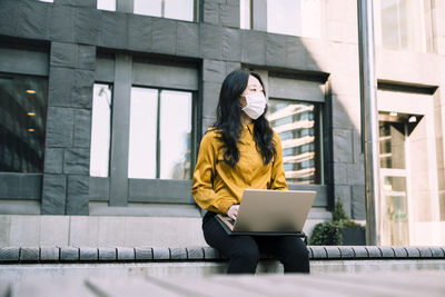 Businesswoman with laptop working outside wearing face mask