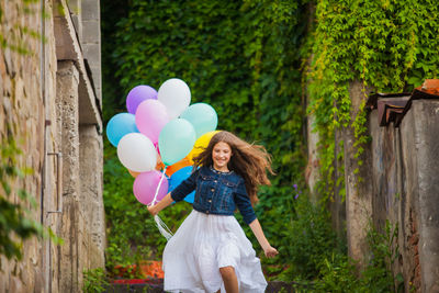 Smiling girl holding balloon running outdoors