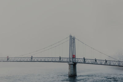 People walking through river on modern bridge with mist on cloudy day