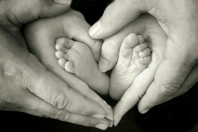 Cropped image of parents making heart shape with baby feet against black background