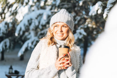 Portrait of young woman standing against winter trees