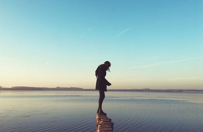 Woman standing on wooden posts at beach against clear sky