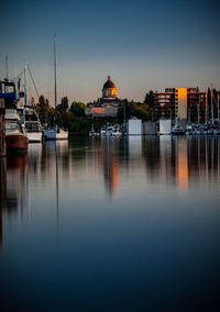 Sailboats moored in illuminated city against sky during sunset